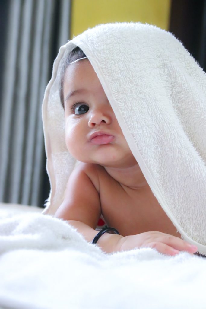 baby with white bath towel draped diagonally over the face